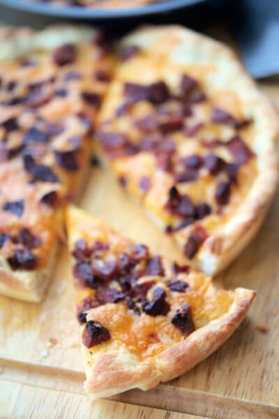 pizza with cheddar and chourico on a wooden cutting board