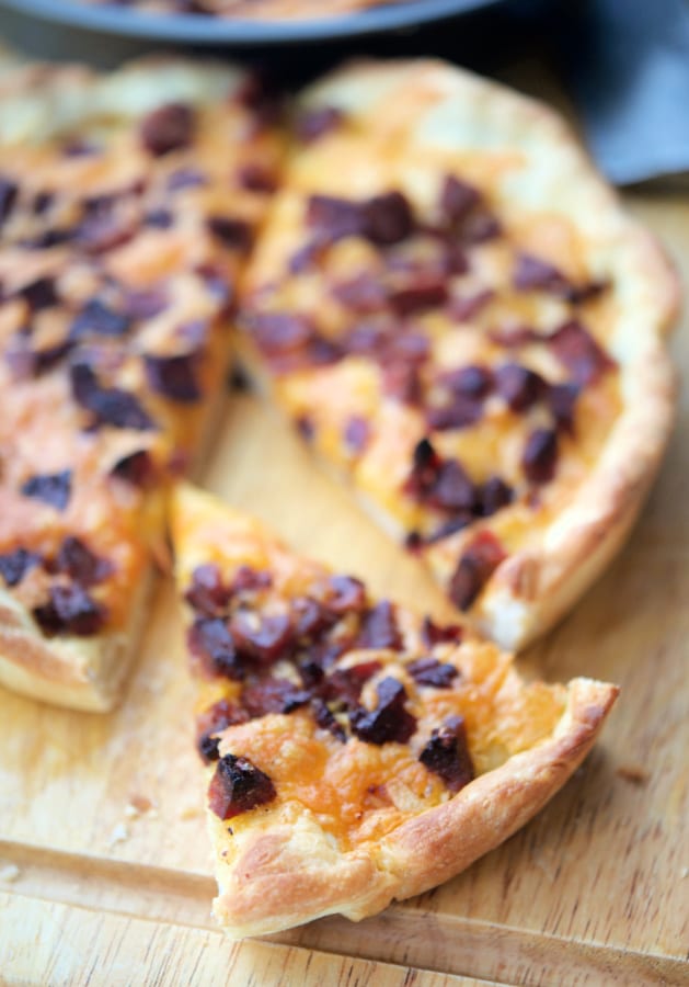 pizza with cheddar and chourico on a wooden cutting board