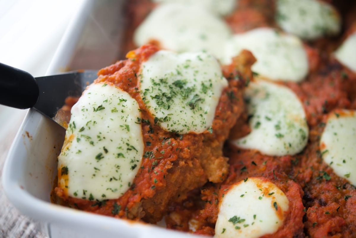 a close up of vodka sauce on breaded chicken in a dish