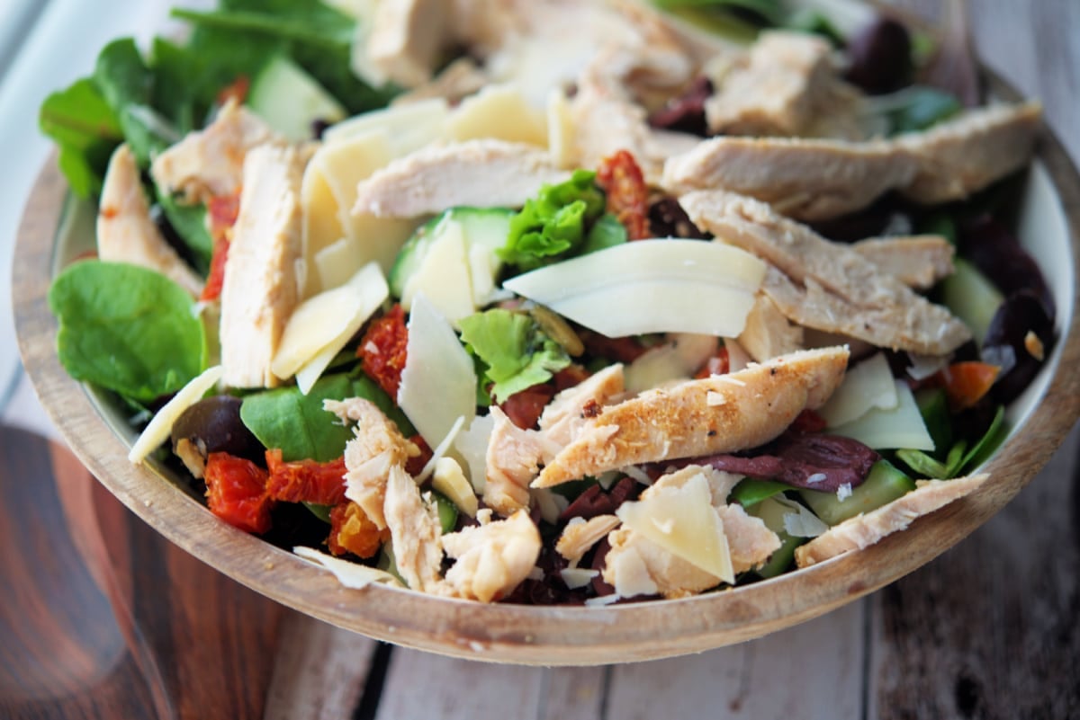 a close up of salad in a bowl with chicken and cheese