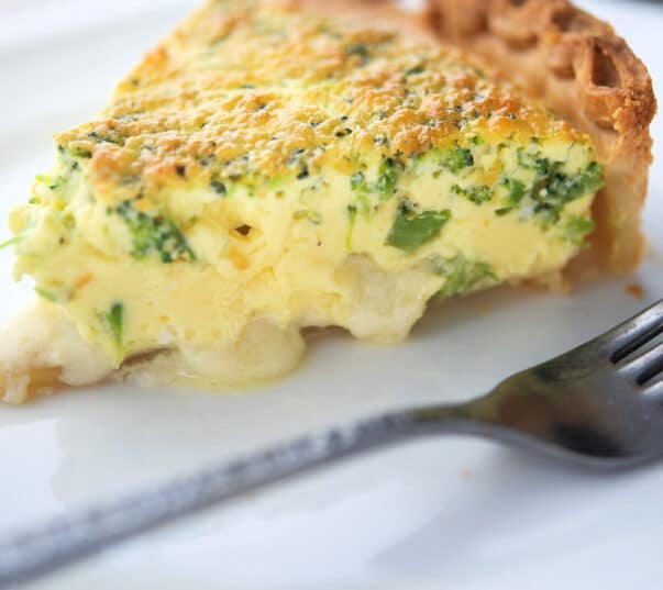 a slice of quiche with broccoli on a white plate