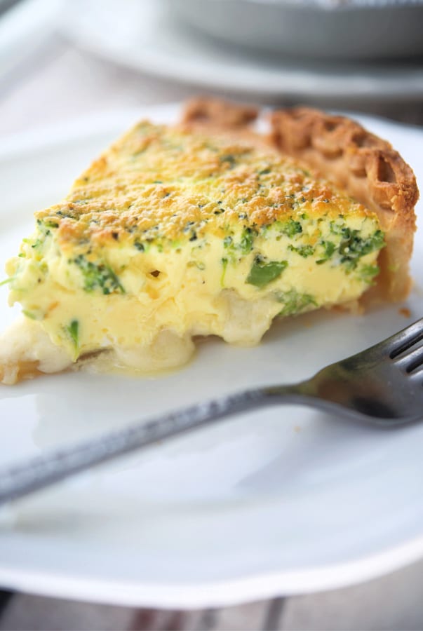 a slice of quiche with broccoli on a white plate