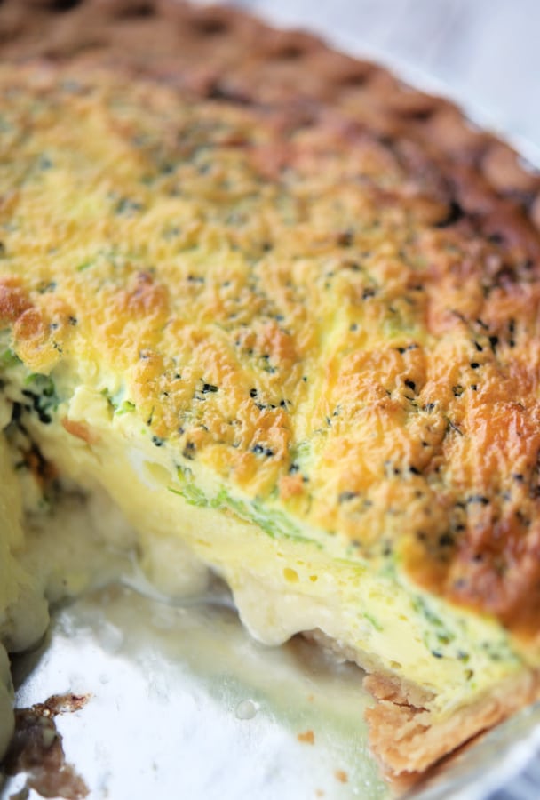 broccoli quiche in a pie dish with a piece cut out