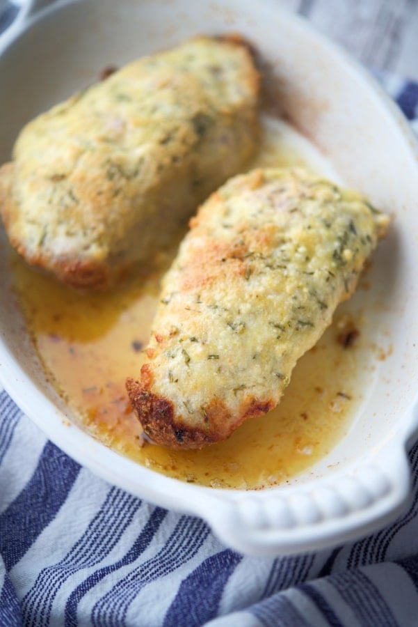 two pork chops crusted with cheese in a white dish