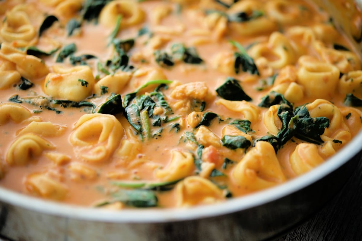 a close up of tortellini with spinach in a pink sauce