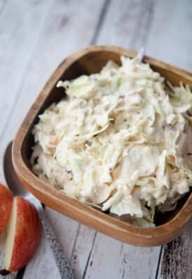 coleslaw with apples in a bowl on a wooden board