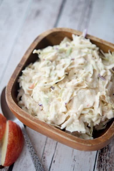 coleslaw with apples in a bowl on a wooden board
