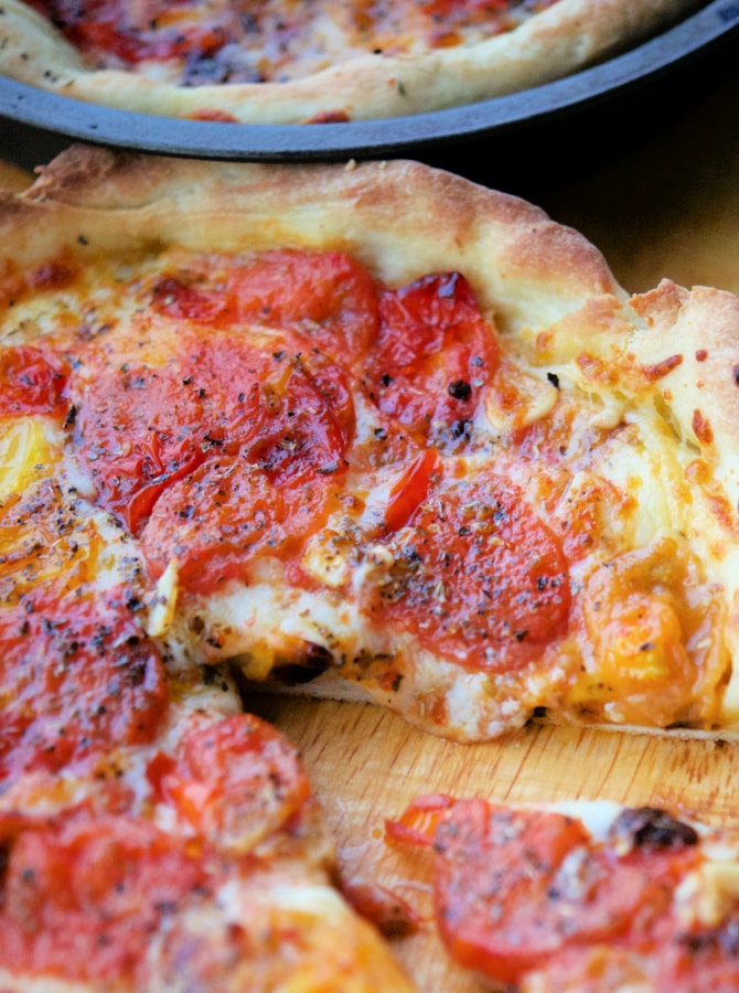 a close up of pizza with tomatoes on a cutting board