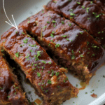 a close up of sliced bbq meatloaf in a white baking dish