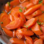 a close up of candied carrots in a stainless steel skillet