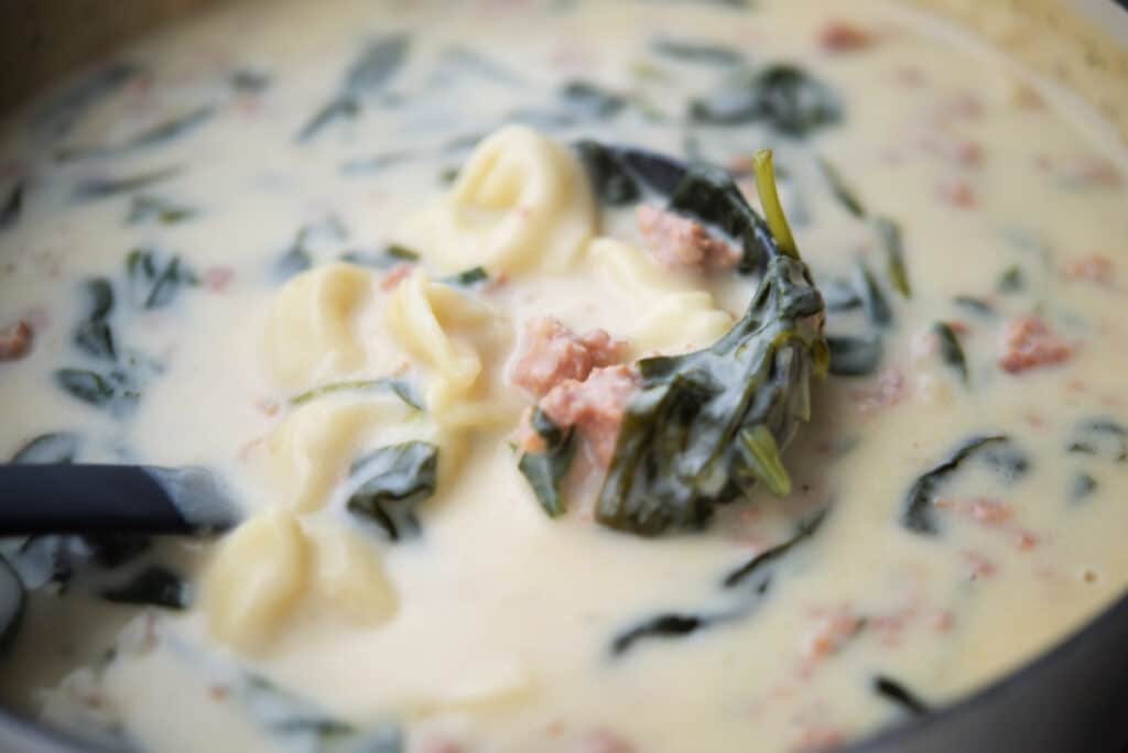 a close up of sausage tortellini soup in a ladle