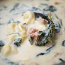 a close up of sausage tortellini soup in a ladle