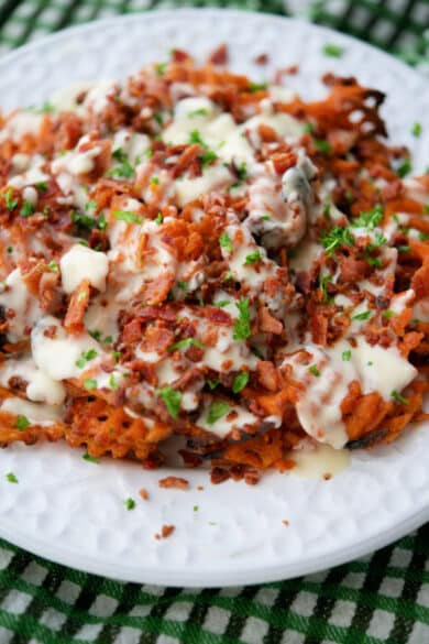 sweet potato waffle fries on a plate with beer cheese sauce and bacon bits