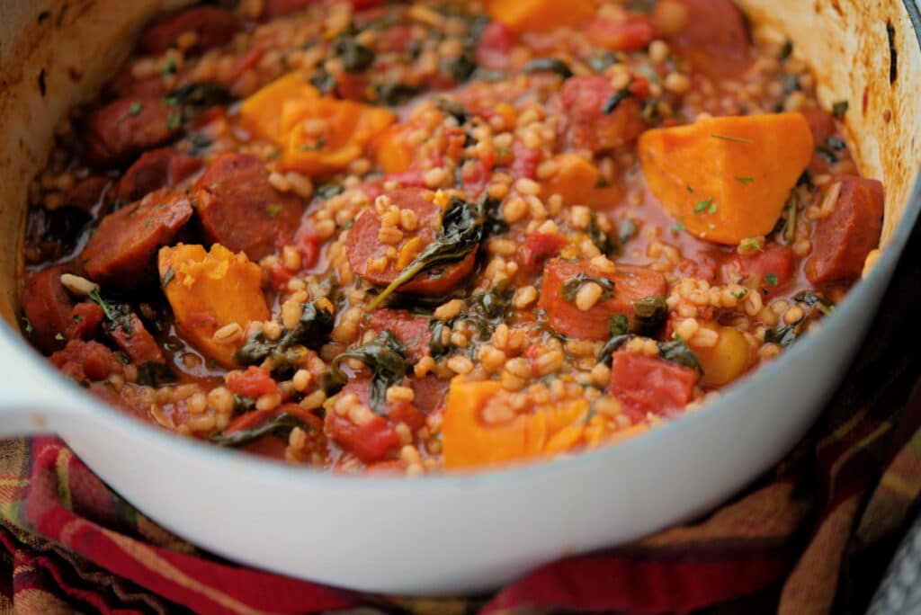 a close up of stew with chourico and sweet potatoes in a white pot