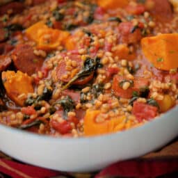 a close up of stew with chourico and sweet potatoes in a white pot