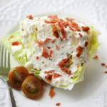 wedge salad on a white plate with dressing and bacon bits