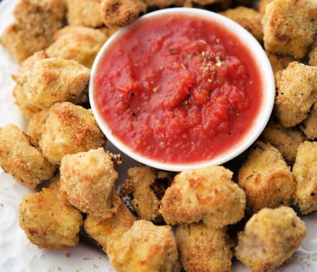italian baked chicken nuggets on a white plate with a dish of marinara sauce