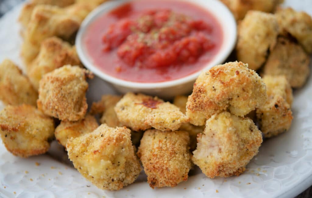 italian style baked chicken nuggets close up on a white plate wth tomato sauce