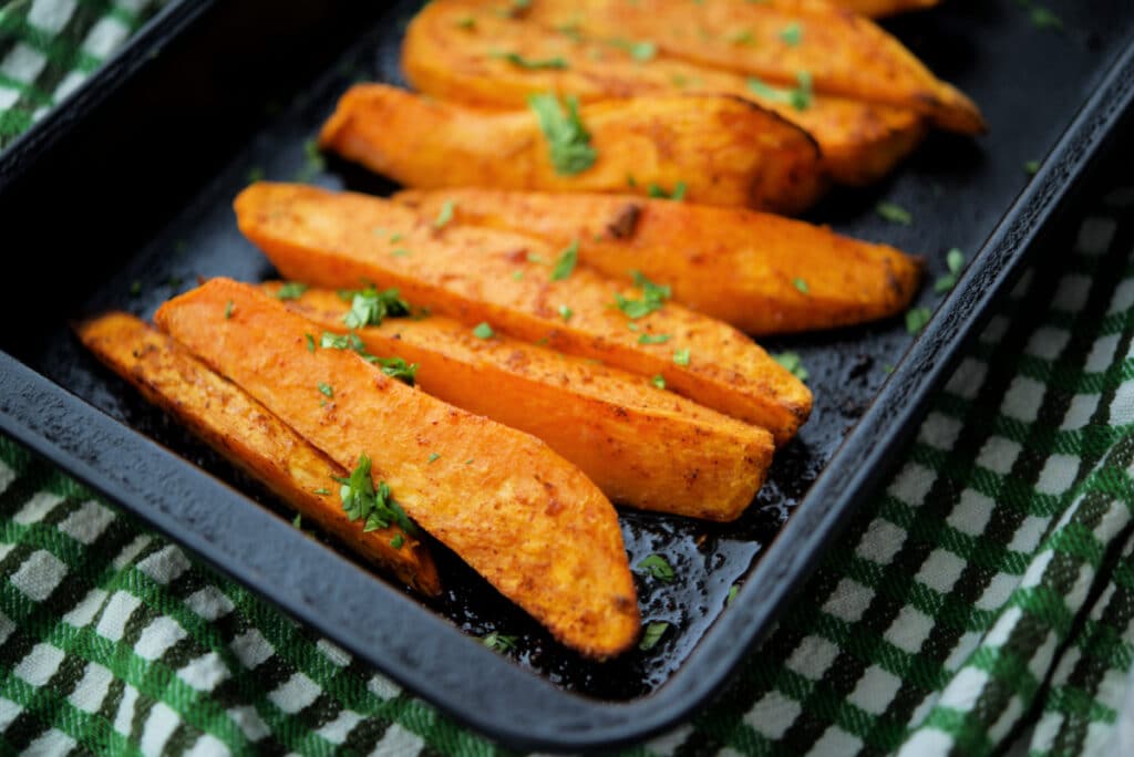 a close up of roasted sweet potato wedges in a small roasting pan