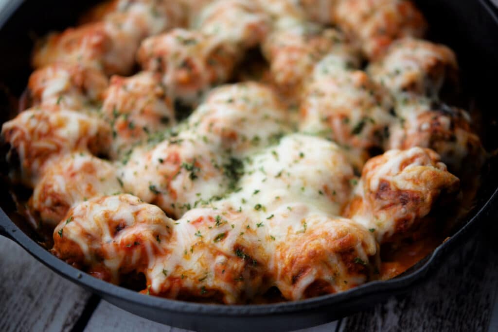 a close up of italian meatballs in vodka sauce with melted cheese