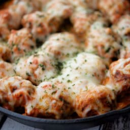 a close up of italian meatballs in vodka sauce with melted cheese