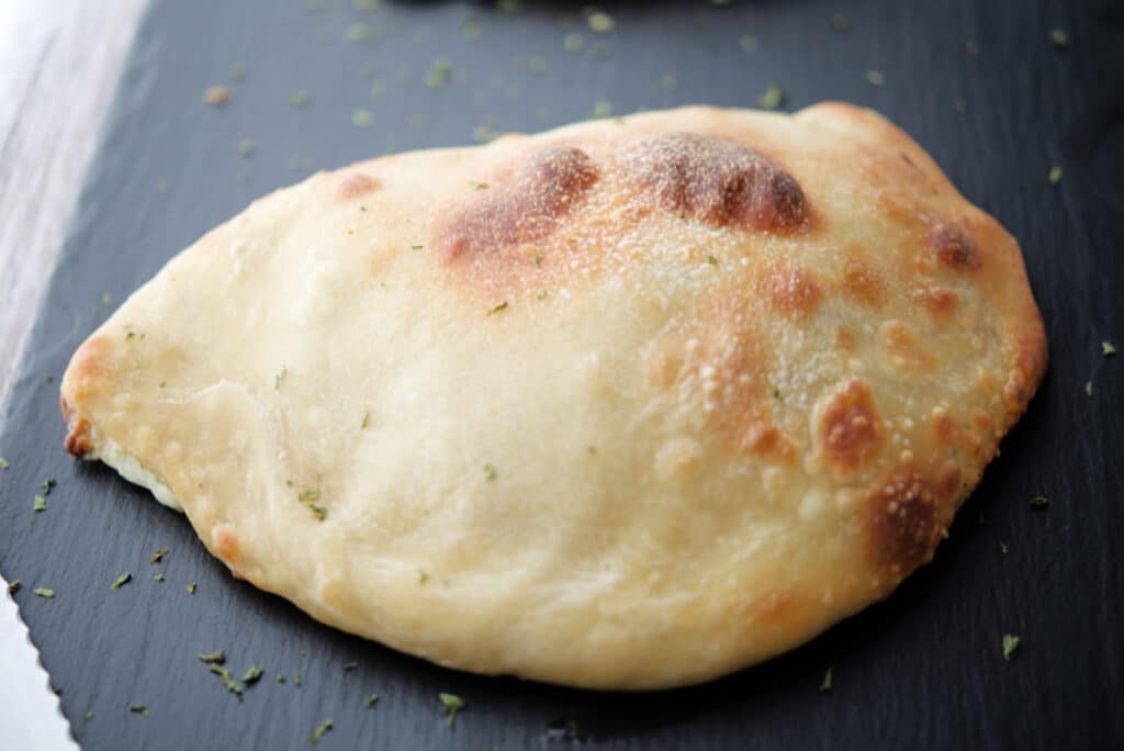 a whole broccoli and cheese calzone on a gray tile