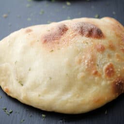 a whole broccoli and cheese calzone on a gray tile