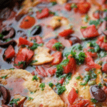 chicken puttanesca in a skillet with olives, tomatoes and capers