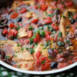 a close up of chicken in a skillet with olives, tomatoes and capers