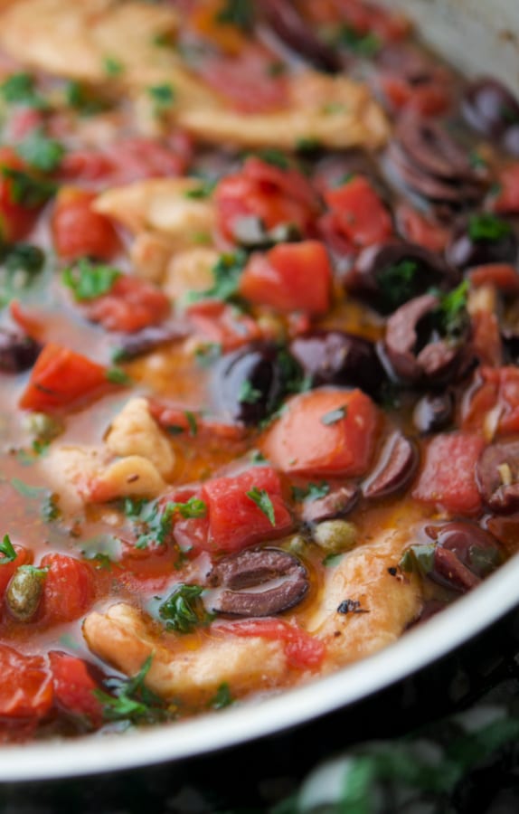 a close up of chicken puttanesca in a skillet