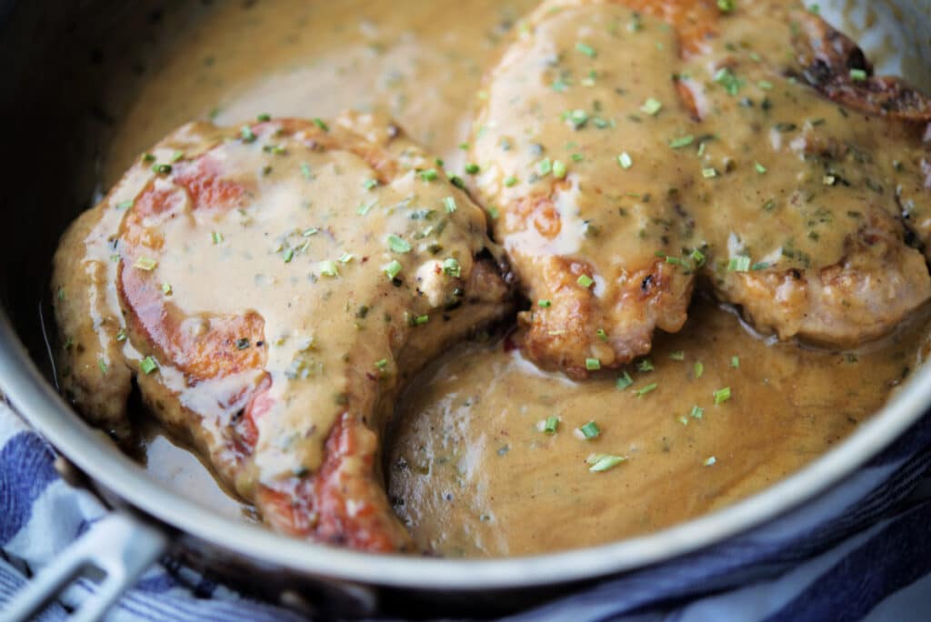close up of bone in pork chops in a skillet with cream sauce