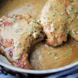 close up of bone in pork chops in a skillet with cream sauce