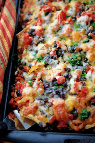 chourico and black bean nachos on a black sheet pan