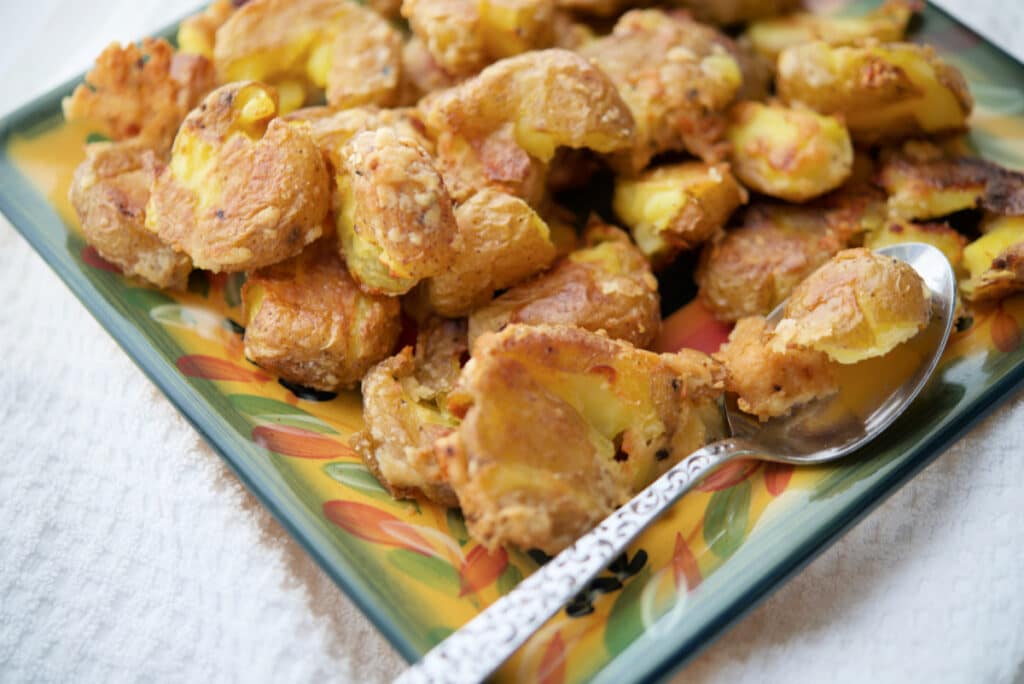 a close up of parmesan smashed potatoes on a plate with a spoon