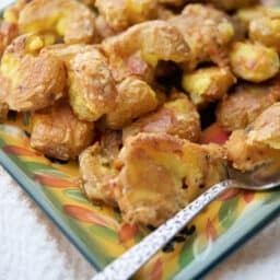 a close up of parmesan smashed potatoes on a plate with a spoon