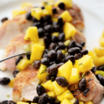 sliced pork chop on a white plate with mango black bean salsa