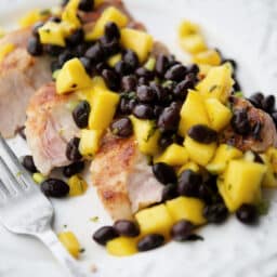 a close up of slice grilled pork chop on a white plate with mango black bean salsa