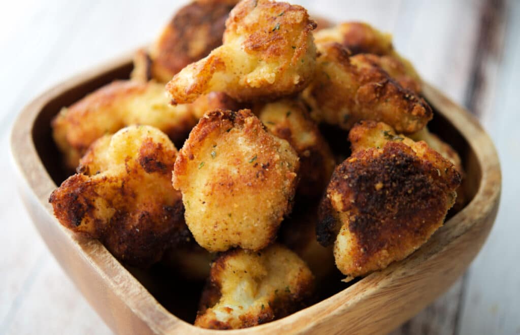 a close up of fried cauliflower in a wooden bowl