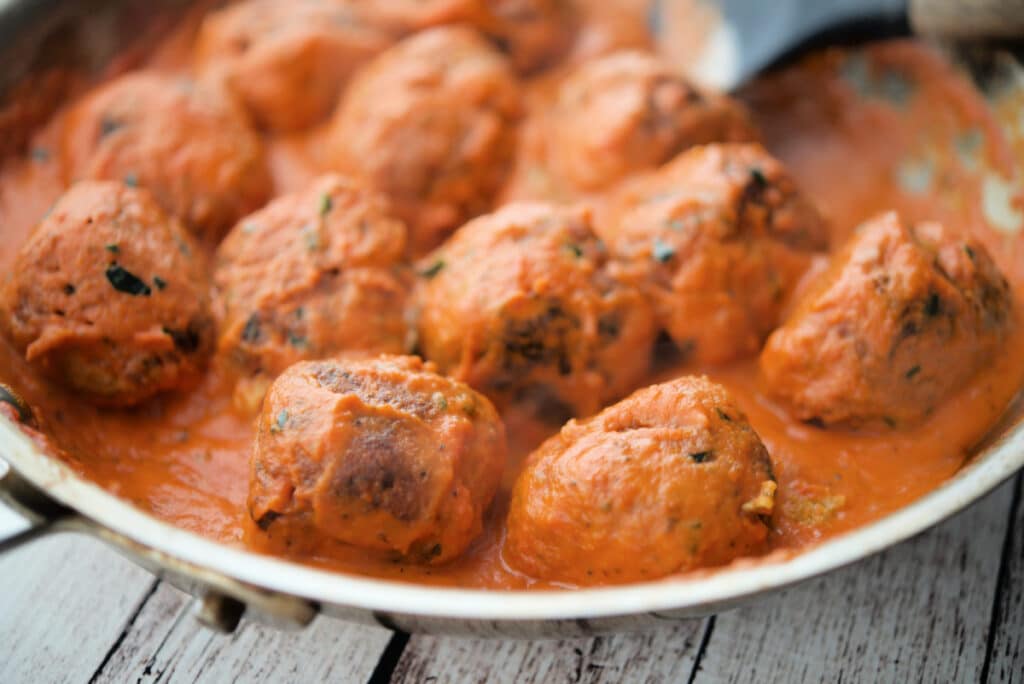 a close up of zucchini meatballs in a pan with vodka sauce