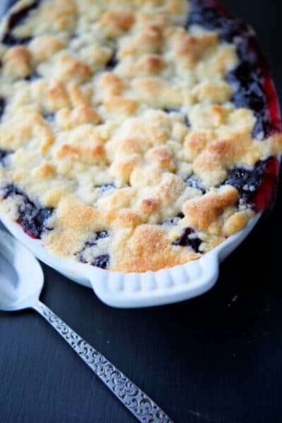 a white dish with baked blueberry pie cobbler