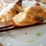 three crab rangooons on a white dish with chopsticks