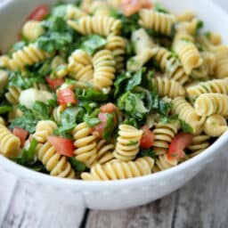 a white bowl with rotini pasta, spinach and artichokes