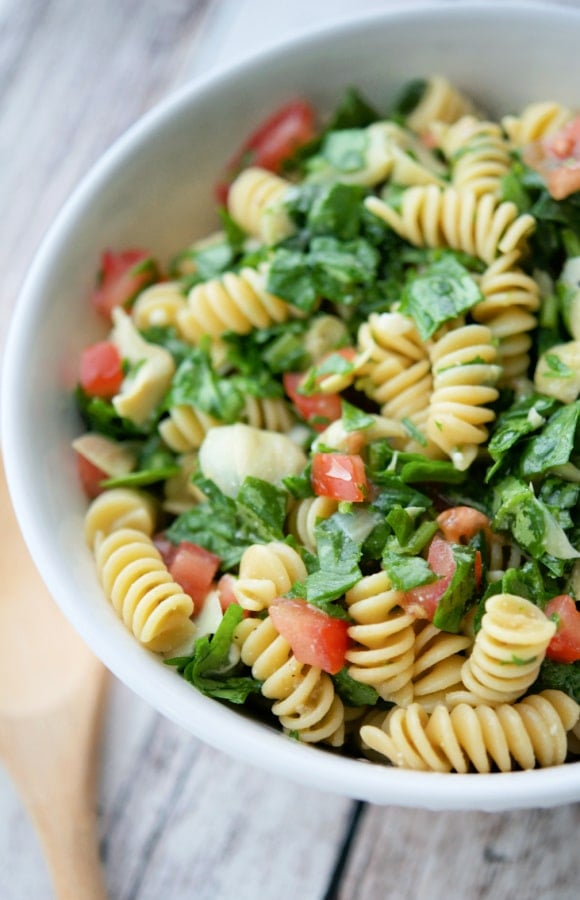 spinach artichoke pasta salad in a white bowl