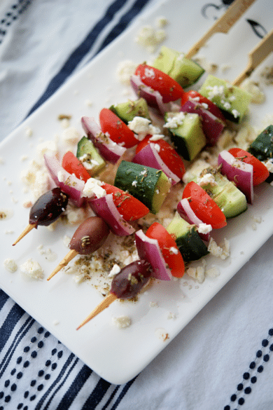 a white plate with four greek appetizer skewers